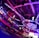 An indoor arena with vibrant purple and blue lighting, featuring large numbered screens suspended from the ceiling. The venue has a high ceiling with intricate metal truss structures and hanging lights, creating a futuristic and energetic atmosphere.